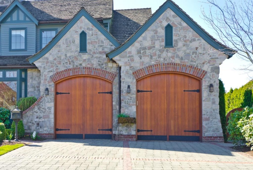 WeServe | Two garage doors with grey brick and brown barn like doors with a paved driveway and the rest of the house in the background
