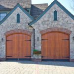 WeServe | Two garage doors with grey brick and brown barn like doors with a paved driveway and the rest of the house in the background
