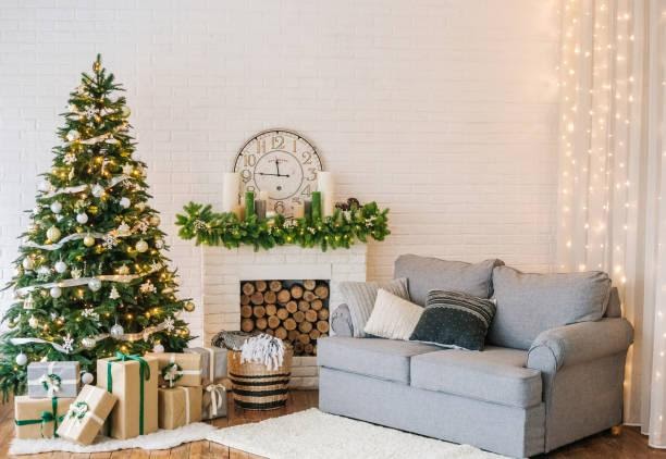 WeServe, a fireplace surrounded by a decorated christmas tree with presents under it and a grey sofa